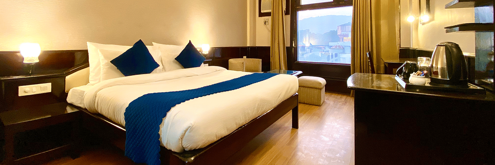 A hotel room with a king size bed, a desk, a chair, a flat-screen TV, and a window with a view of a lake  | DLS Park Grace, Haridwar
